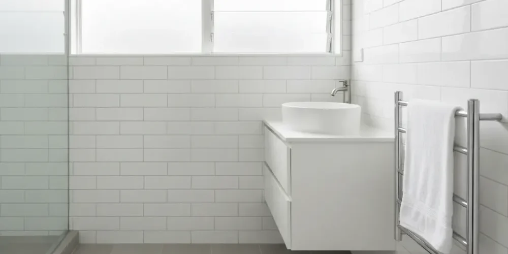 Completed Auckland ensuite renovation with grey stone-look tiles, white subway walls, vessel basin, and chrome heated towel rail.